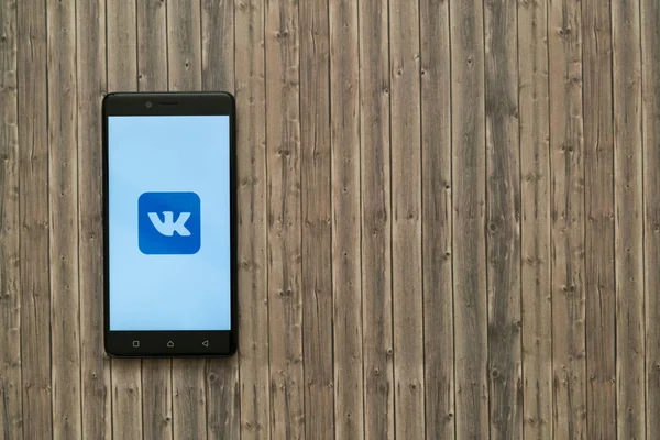 Logotipo de Vkontakte en la pantalla del teléfono inteligente sobre fondo de madera . — Foto de Stock