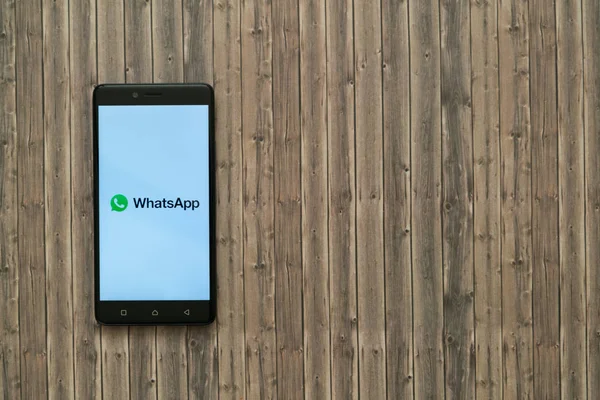 Logo de Whatsapp en la pantalla del teléfono inteligente sobre fondo de madera . —  Fotos de Stock