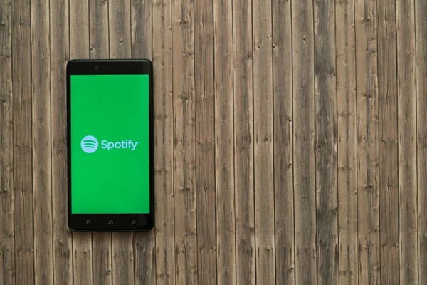 Spotify λογότυπο στην οθόνη του smartphone σε φόντο ξύλινη. — Φωτογραφία Αρχείου