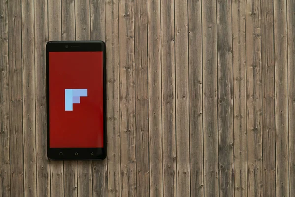 Logotipo de Flipboard en la pantalla del teléfono inteligente sobre fondo de madera . — Foto de Stock