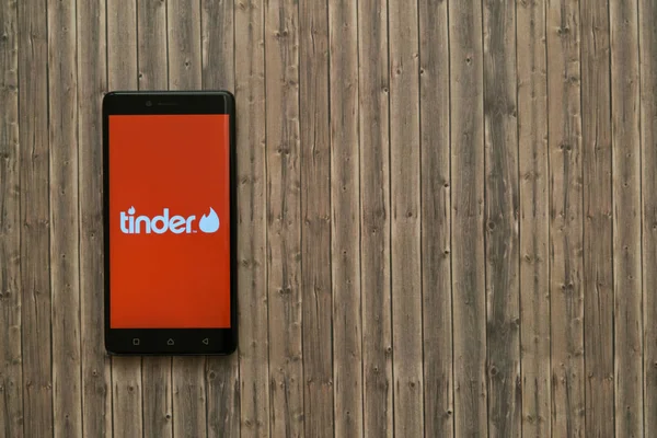 Tinder-logo op het scherm van de smartphone op houten achtergrond. — Stockfoto