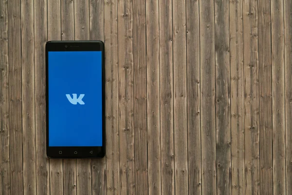 Logotipo de Vkontakte en la pantalla del teléfono inteligente sobre fondo de madera . — Foto de Stock