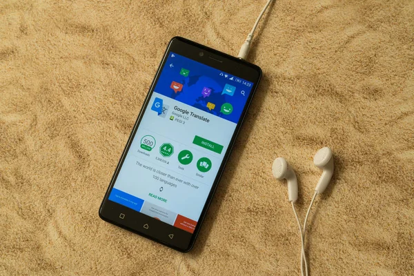 Aplicación de traductor de Google en Google Play Store sobre fondo arenoso y auriculares — Foto de Stock