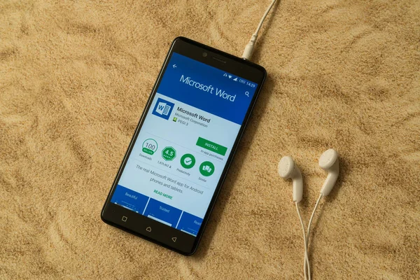 Microsoft Word application in google play store on sandy background and earphones — стоковое фото