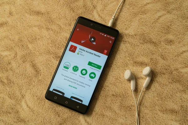 Adobe Acrobat Reader Anwendung in Google Play Store auf sandigem Hintergrund und Kopfhörer — Stockfoto