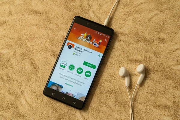 Applicazione Retrica in Google Play Store su sfondo sabbioso e auricolari — Foto Stock