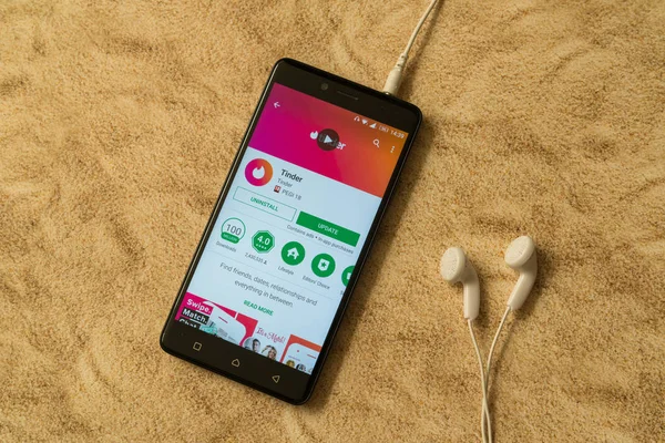 Приложение Tinder в Google Play Store на песчаном фоне и наушниках — стоковое фото