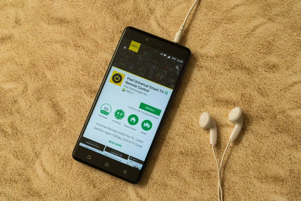 Pelar universal smart tv aplicación de control remoto en Google Play Store sobre fondo arenoso y auriculares — Foto de Stock