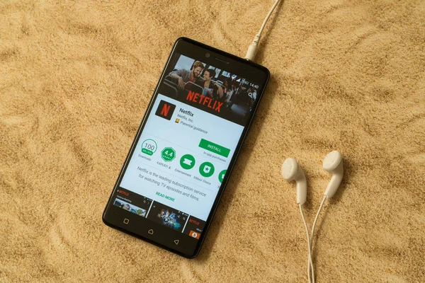 Netflix приложение в Google Play Store на песчаном фоне и наушниках — стоковое фото