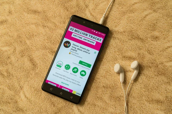 London, 14. November 2017: Deezer-Anwendung im Google Play Store auf sandigem Hintergrund und Kopfhörer — Stockbild Deezer-Anwendung im Google Play Store auf sandigem Hintergrund und Kopfhörer — Stockfoto