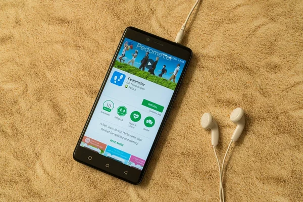 Schrittzähler-Anwendung in Google Play Store auf sandigem Hintergrund und Kopfhörer — Stockfoto