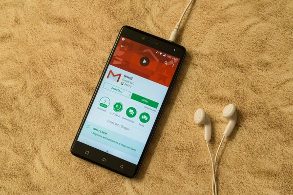Gmail-Anwendung in Google Play Store auf sandigem Hintergrund und Kopfhörer — Stockfoto