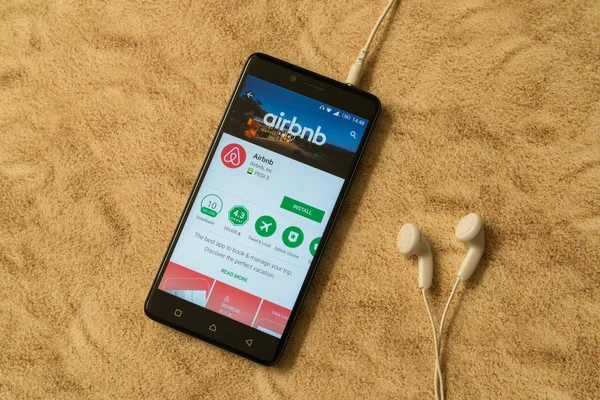 Aplicación Airbnb en Google Play Store sobre fondo arenoso y auriculares — Foto de Stock