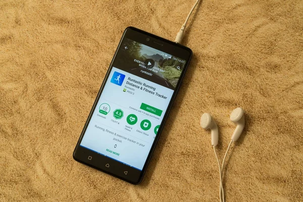Runtastic application in google play store on sandy background and earphones — Stock Photo, Image