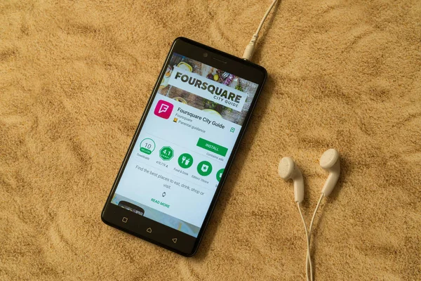 Aplicación Foursquare en Google Play Store sobre fondo arenoso y auriculares — Foto de Stock