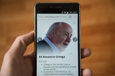 Londra, 31 Aralık 2017: Amancio Ortega forbes Web, cep telefonu sürümü. El ahşap arka plan ile akıllı telefon tutarak