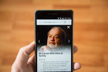 Londra, 31 Aralık 2017: Carlos Slim Helu forbes Web, cep telefonu sürümü. El ahşap arka plan ile akıllı telefon tutarak