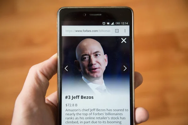 Londra, 31 Aralık 2017: Jeff Bezos forbes Web, cep telefonu sürümü. El ahşap arka plan ile akıllı telefon tutarak