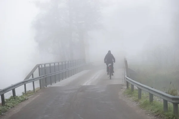 暗い秋の日に重い霧の中で橋の上にサイクリストの後部ビブ — ストック写真