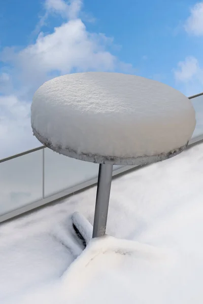Small round metal table with snow in top, on blue sky