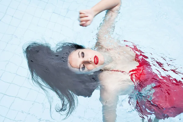 Vrouw in een rode jurk, zwemmen in het zwembad — Stockfoto