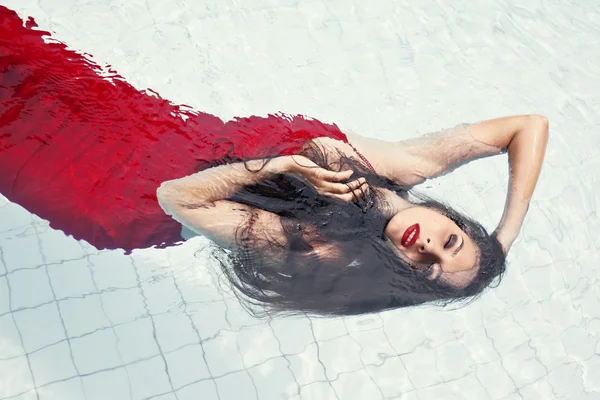Kvinna i en röd klänning som simmar i poolen — Stockfoto