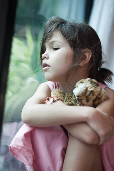 Dívka sedí u okna s hračkou — Stock fotografie