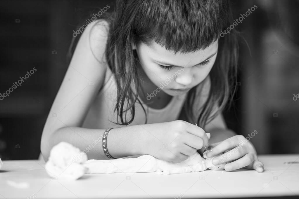 Focused little girl sculpting pottery human statue sitting at table
