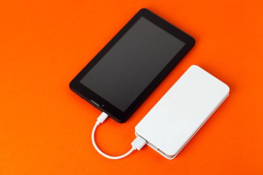 Tablet bilgisayar üzerinden harici pil, turuncu bir arka plan üzerinde kullanılıyorsa.