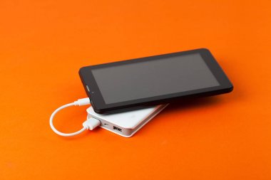 Tablet bilgisayar üzerinden harici pil, turuncu bir arka plan üzerinde kullanılıyorsa.