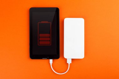 The tablet computer is charged from an external battery, on an orange background. clipart