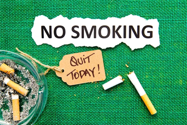 Proibido fumar - com cinzeiro, cigarro quebrado, etiqueta manuscrita e texto impresso em fundo de serapilheira verde — Fotografia de Stock