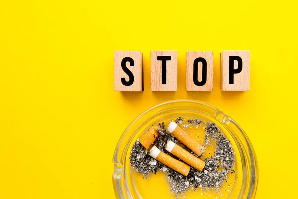 Pare de fumar - bloquear letras de madeira com cinzeiro no fundo amarelo — Fotografia de Stock