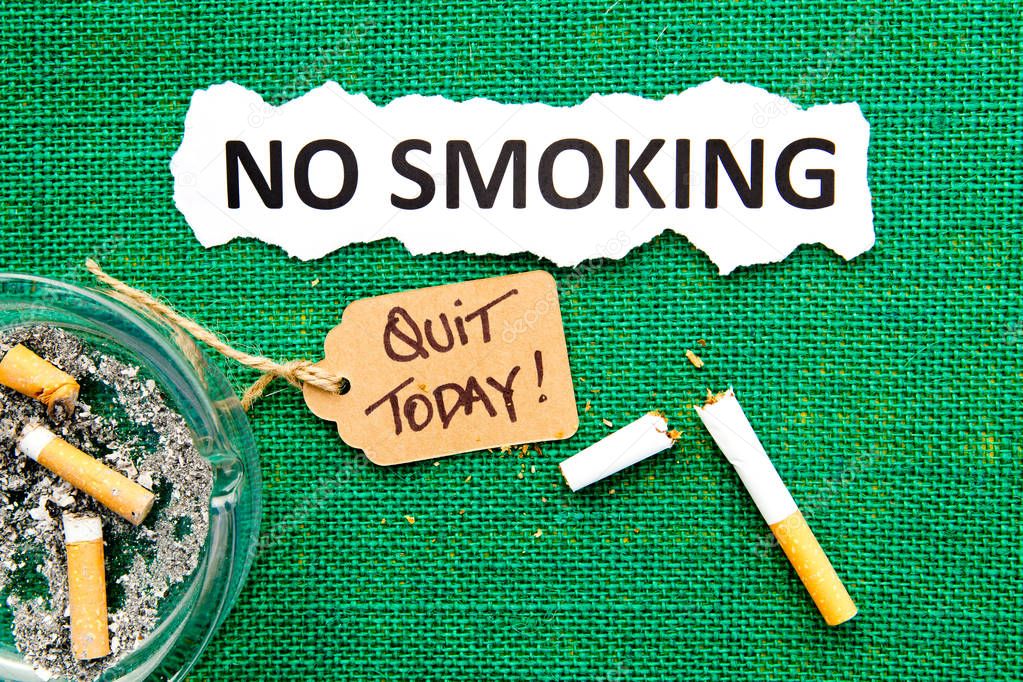 No Smoking - with ashtray, broken cigarette, handwritten tag and printed text on green burlap background