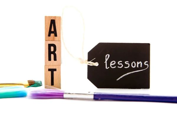 Art - blocks and brushes on white background with lessons handwritten on chalkboard tag — Stock Photo, Image