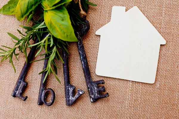 Láska klíče s domem a byliny na pozadí pytlovina — Stock fotografie