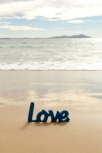 Niebieski słowo miłość drewniana piasku w fale na plaży — Zdjęcie stockowe