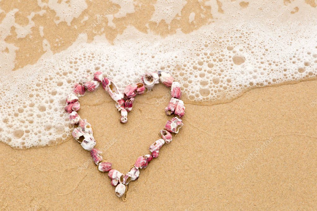 Heart shape in pink sea shells on beach