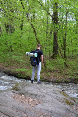 Şık gencin sırt çantası ayakta nehir banka yakındaki bir kayanın üzerinde taşıyan