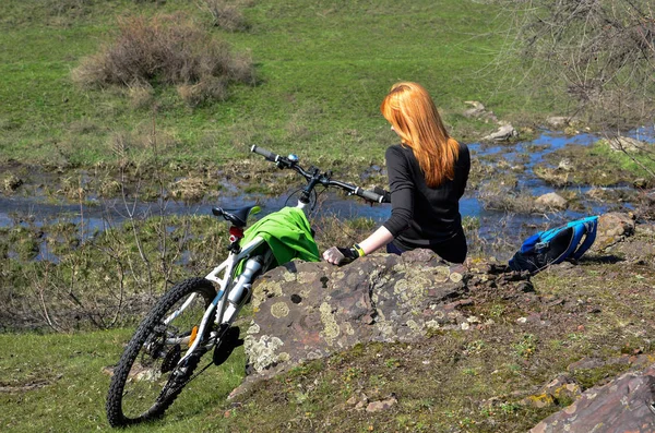 A kerékpár- és lyubuetsya táj egy rock ül a fiatal vörös hajú lány — Stock Fotó