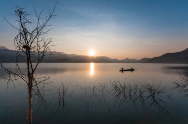 Motorlu tekne gölde gün doğumu ve dağ manzarası ile çalışıyor.