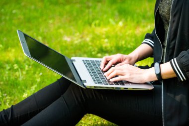 Bir kadınla çimenlerin üzerinde dizüstü bilgisayar kullanırken oturuyor
