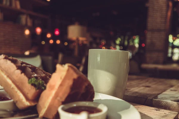 Hot mocha coffee in white cup and blurred waffle on the wooden table — Stock Photo, Image