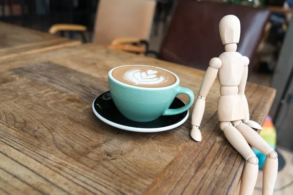 Heißer Mokkakaffee oder Capuchino in der grünen Tasse mit einem Mann aus Holz auf dem Holztisch — Stockfoto
