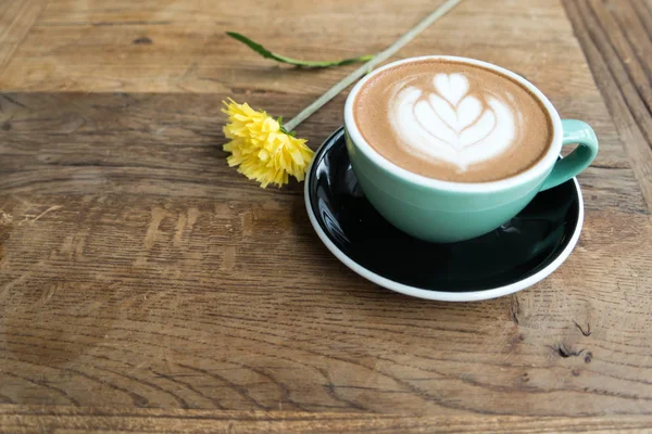 Sıcak mocha kahve veya capuchino ahşap masa üzerinde kalp desen ve Sarı çiçekli yeşil Kupası