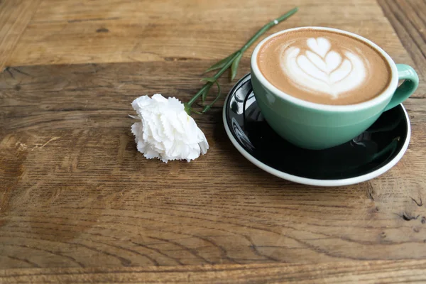 Caffè caldo moka o capuchino nella tazza verde con motivo a cuore e garofano bianco sul tavolo di legno — Foto Stock