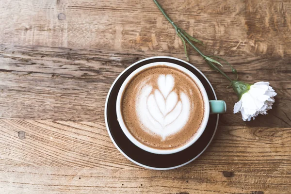 Sıcak mocha kahve veya capuchino ile kalp desen ve beyaz Karanfil ahşap masa üzerinde yeşil Kupası