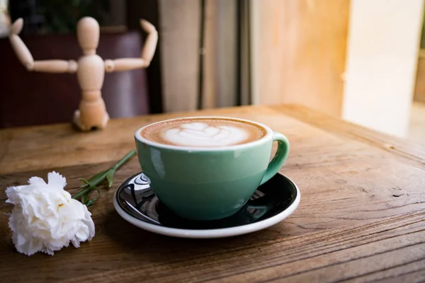 Café mocha quente ou capuchino com flor de cravo branco e homem de madeira na mesa de madeira — Fotografia de Stock