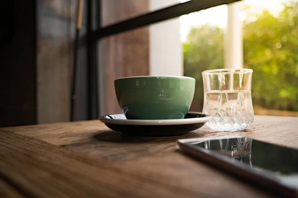 コーヒー カップと木製のテーブルにスマート フォンが付いている水のガラス — ストック写真