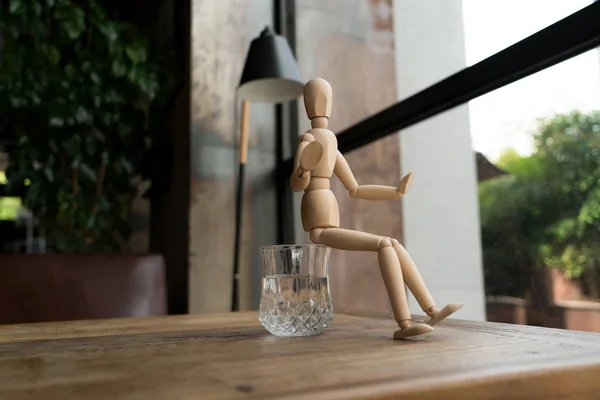 Homem de madeira está sentado em um copo de água — Fotografia de Stock